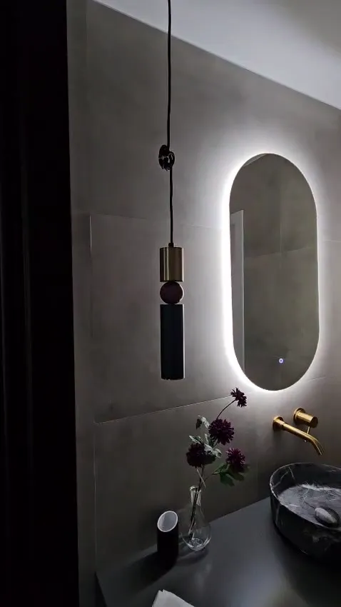 Baño terminado: espejo ovalado retroiluminado, grifería dorada y lavabo de piedra